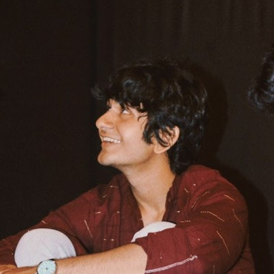 Yashank Kothari, smiling and looking up, in a dark red shirt against a black curtain